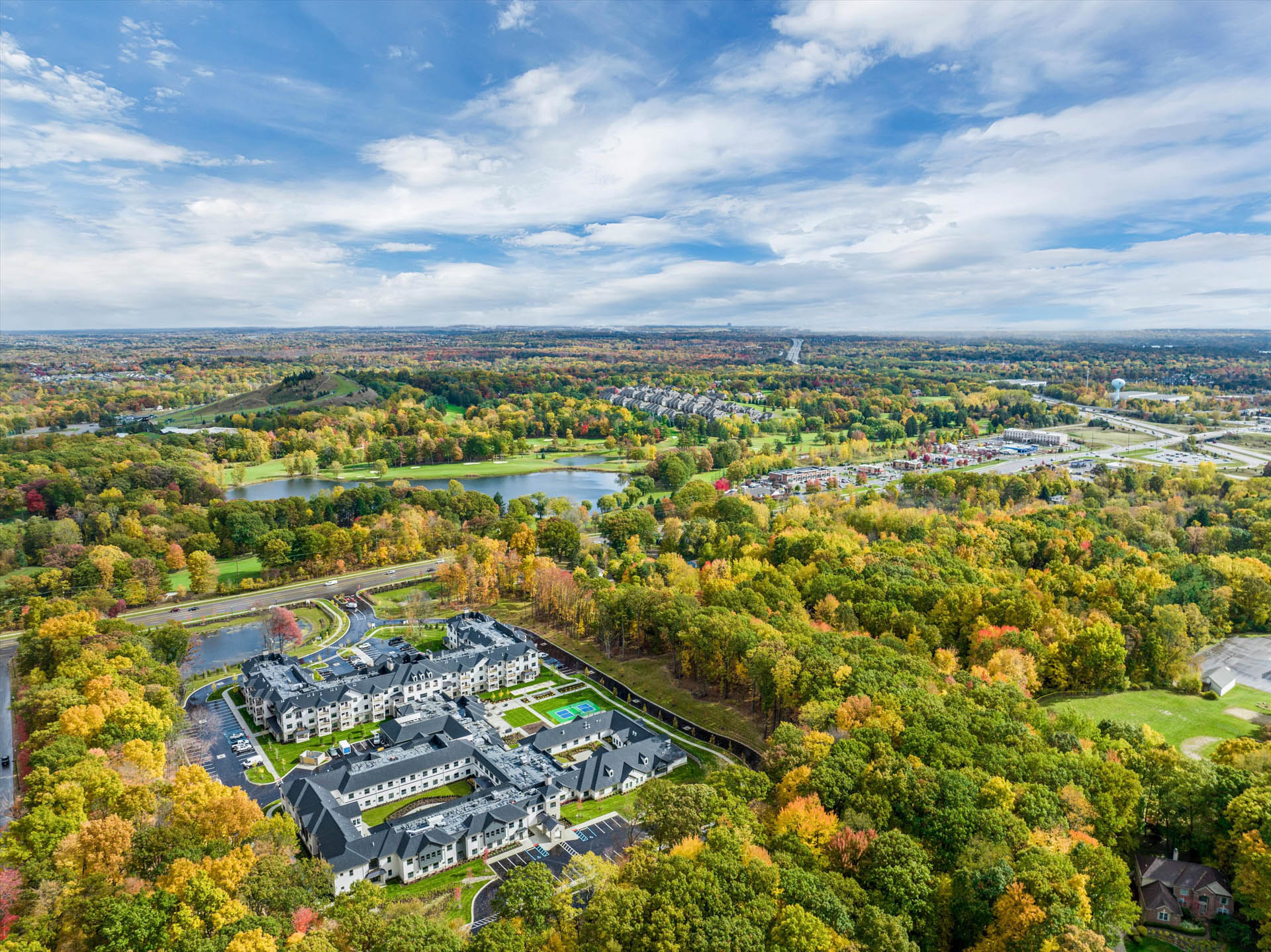 Aerial view of a senior living community surrounded by wooded landscape and autumn foliage.