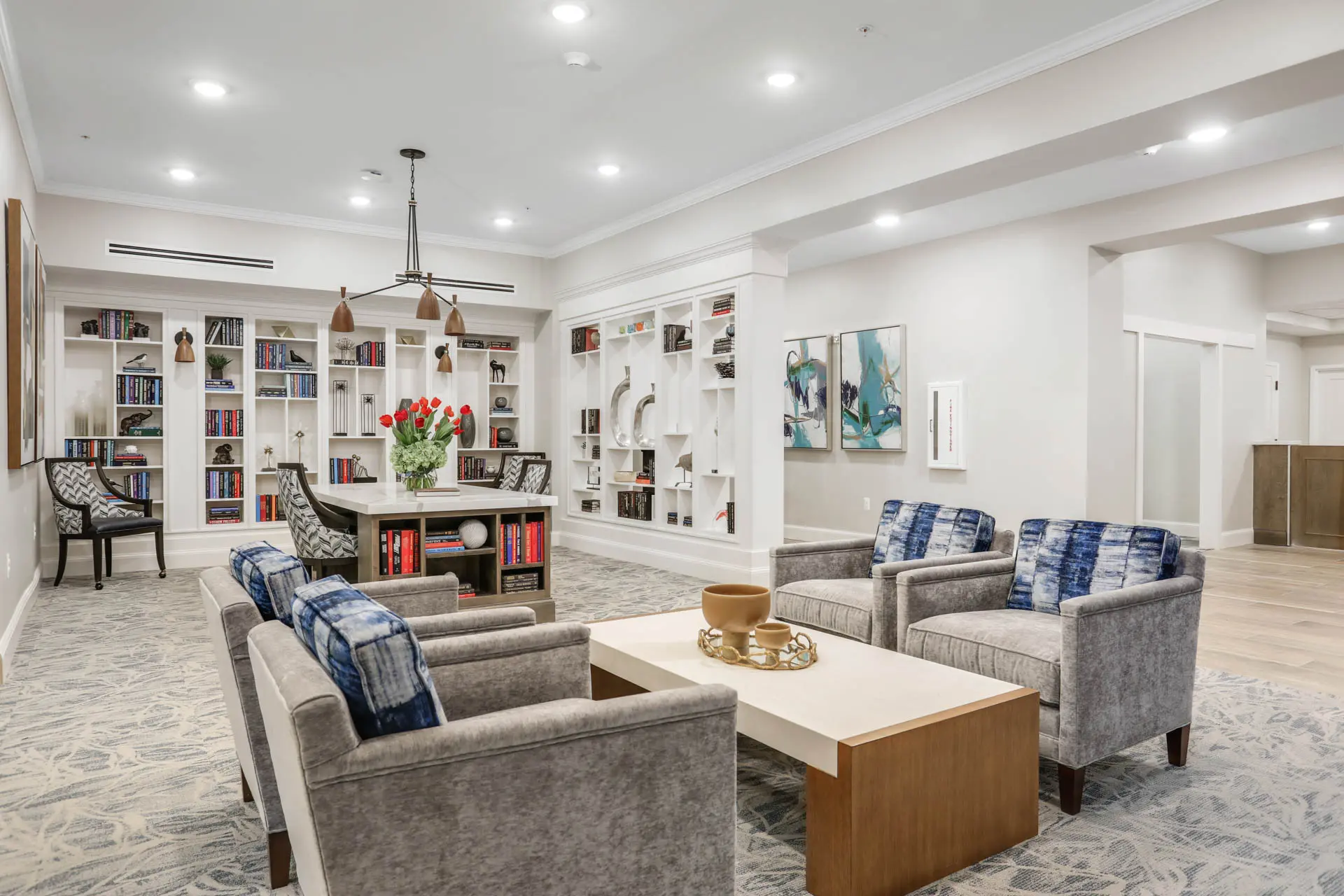 Senior living lounge with built-in bookshelves, armchairs and central reading table.
