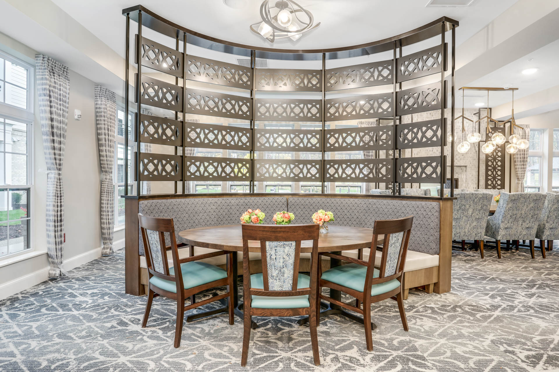 Senior living dining area with round table, upholstered booth seating and decorative privacy screen.