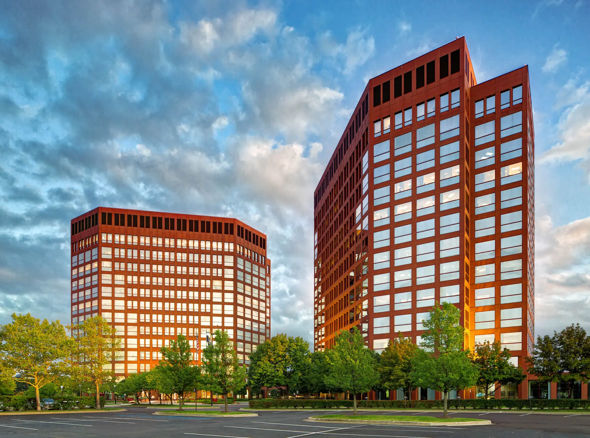 Two multi-story commercial office towers surrounded by landscaped grounds at dusk.