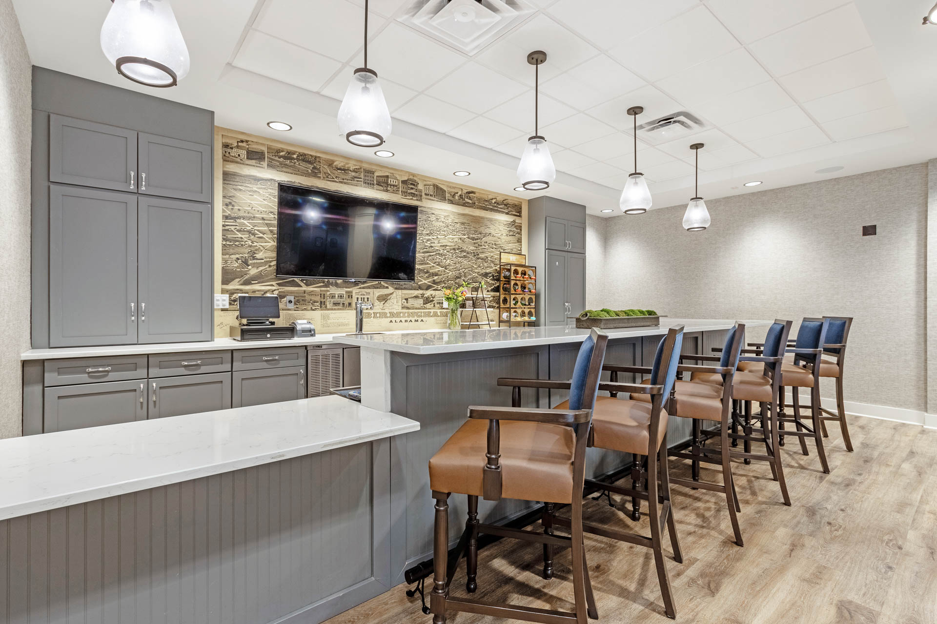 Senior living dining and lounge area with counter seating, pendant lights and wall-mounted television.