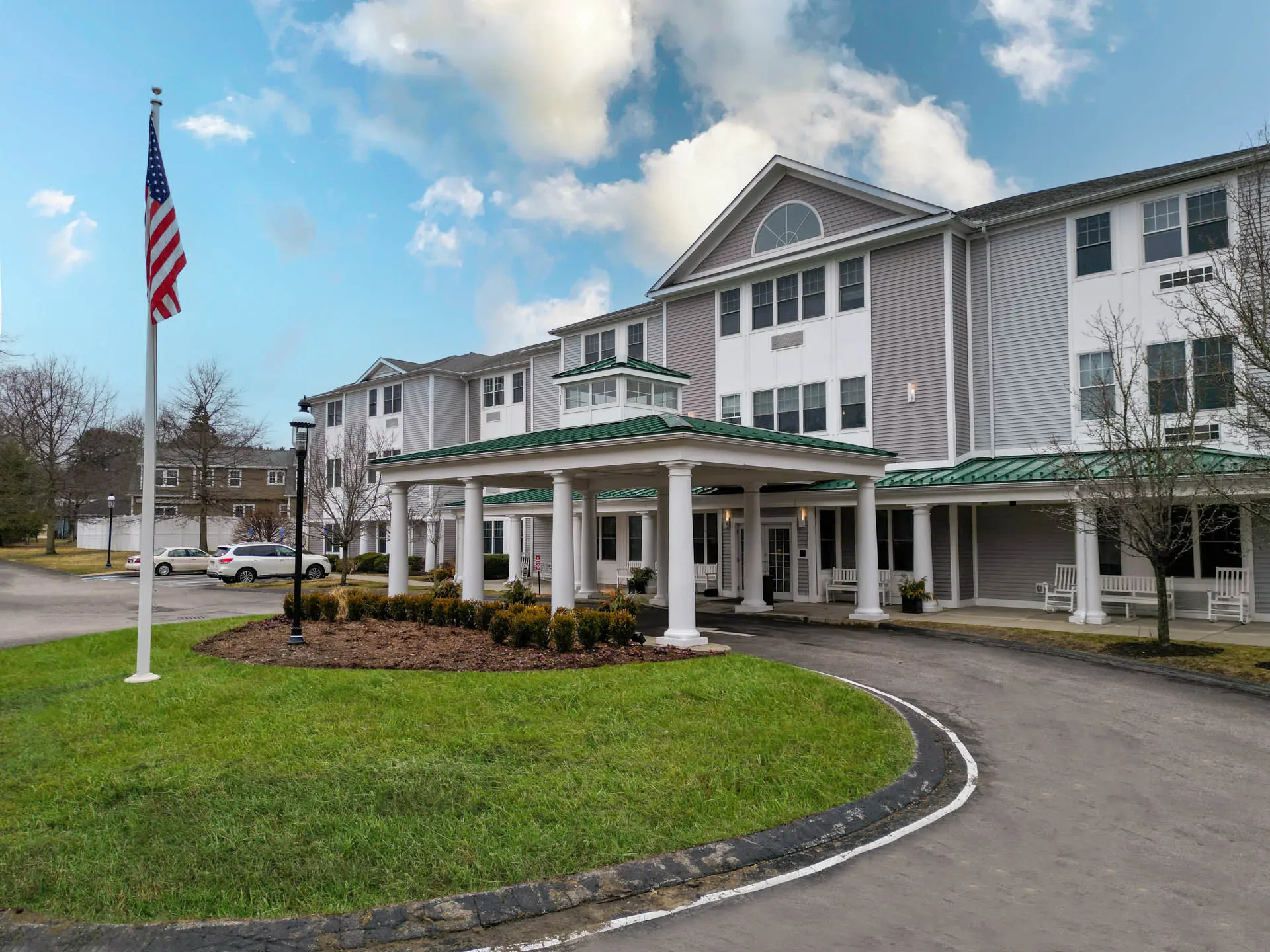 Multi-story senior living community with covered entrance, landscaped grounds and American flag.