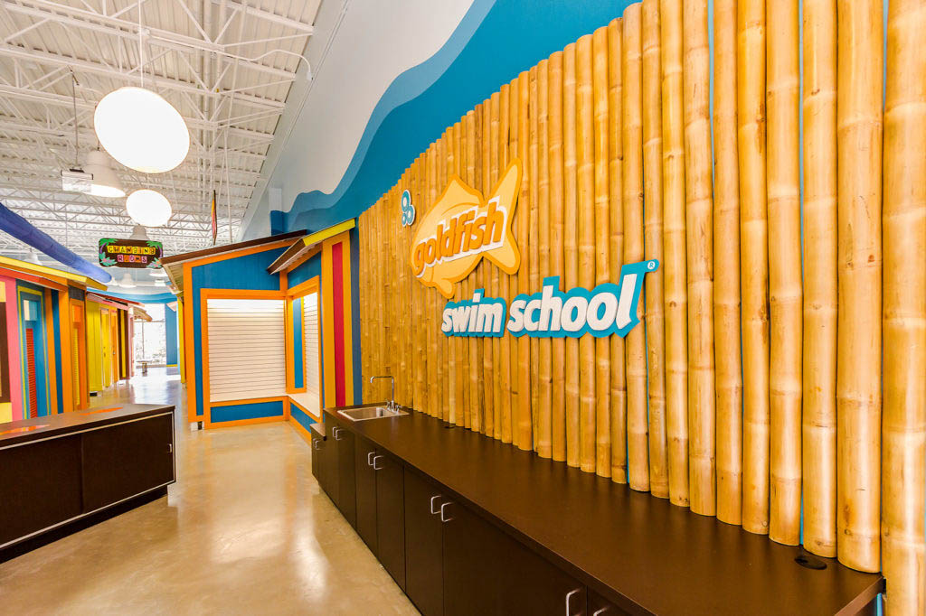 Colorful Goldfish Swim School interior with bamboo accent wall and branded signage.