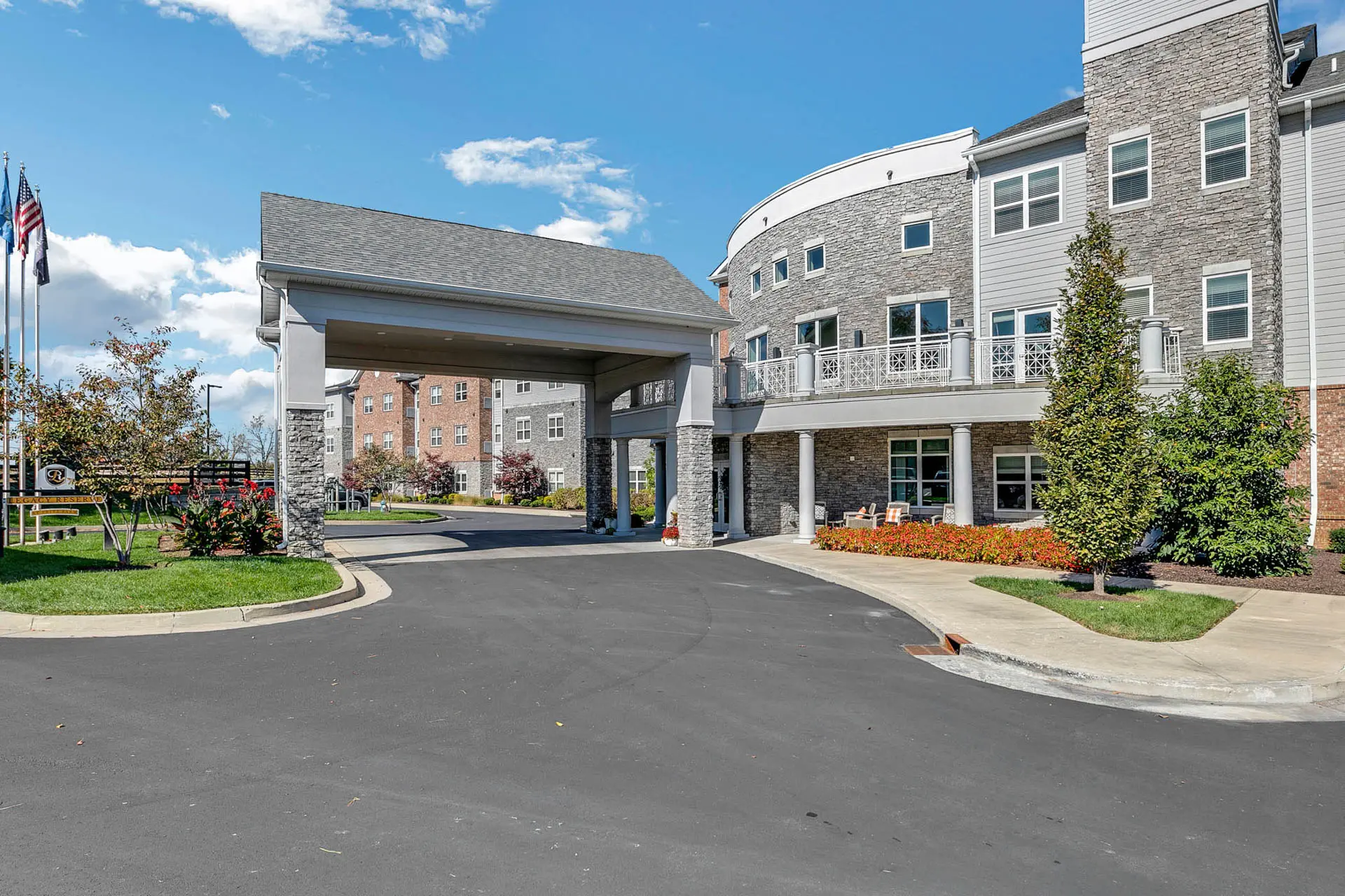 Senior living community exterior with stone façade, covered entrance and landscaped grounds.