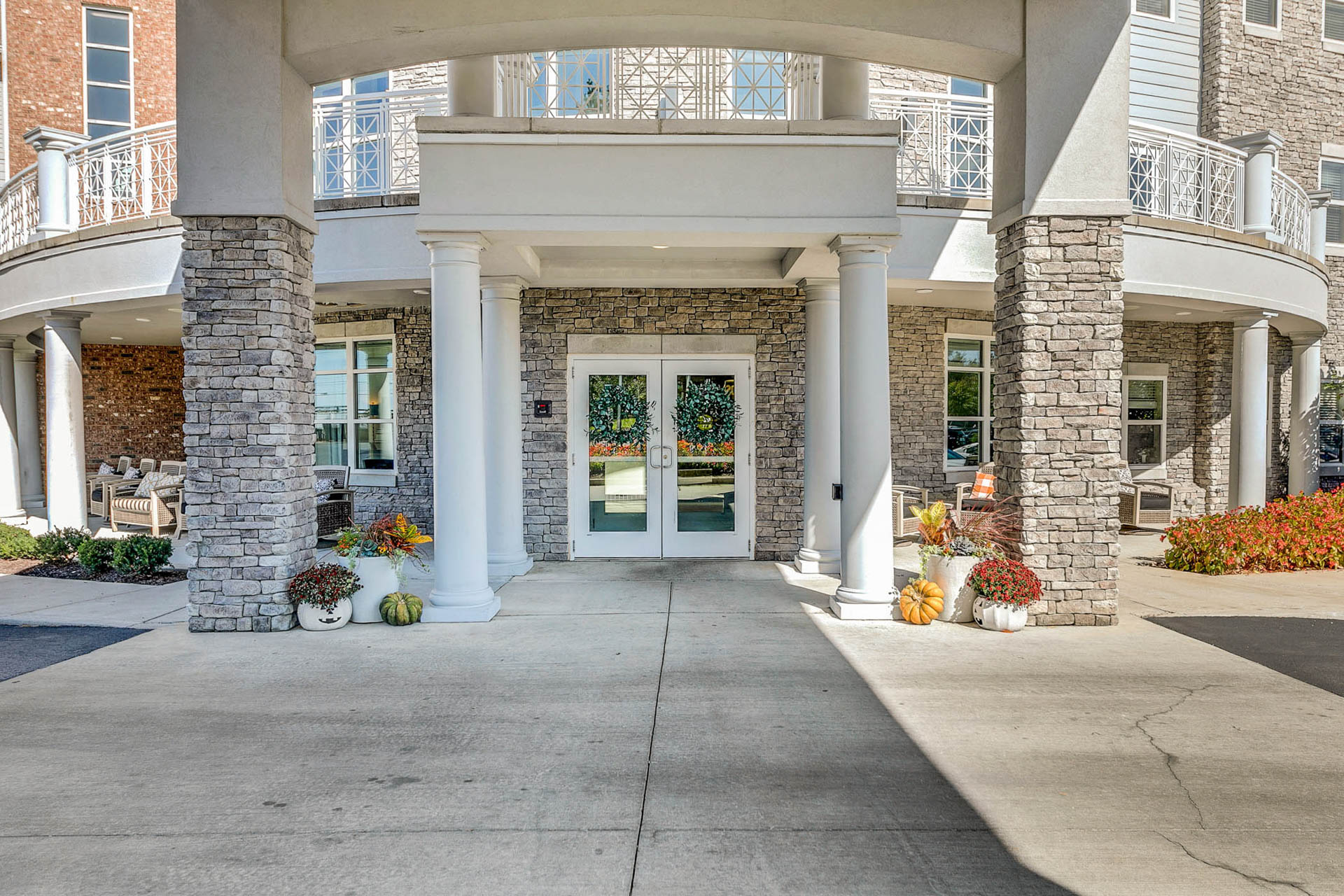 Covered entrance to a senior living community with stone columns and outdoor seating.