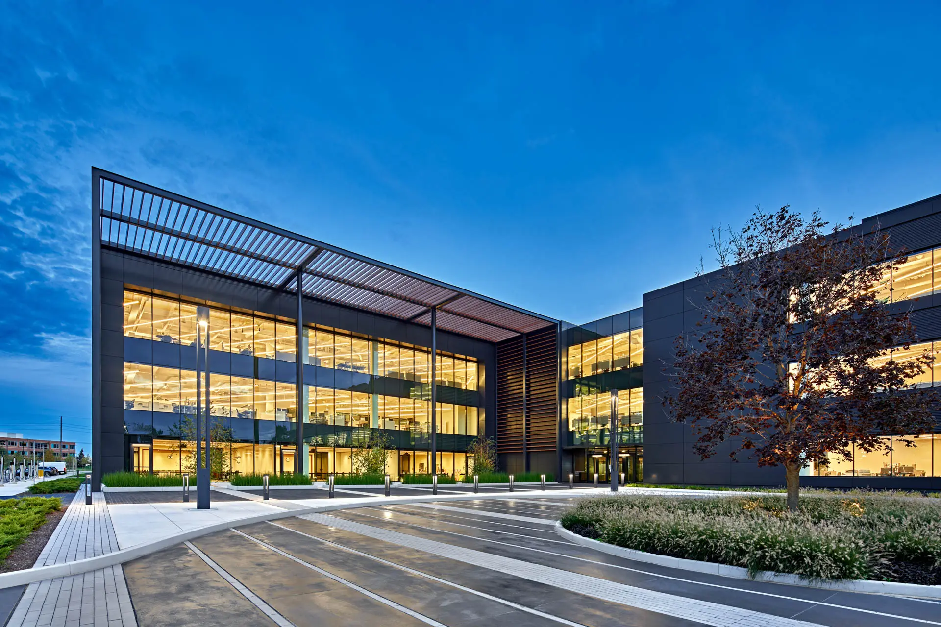Modern corporate office building with expansive glass walls and illuminated interior at dusk.