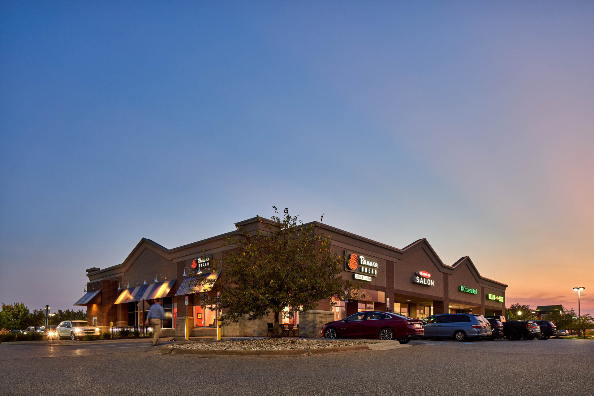 Retail center featuring Panera Bread and neighboring storefronts at sunset.