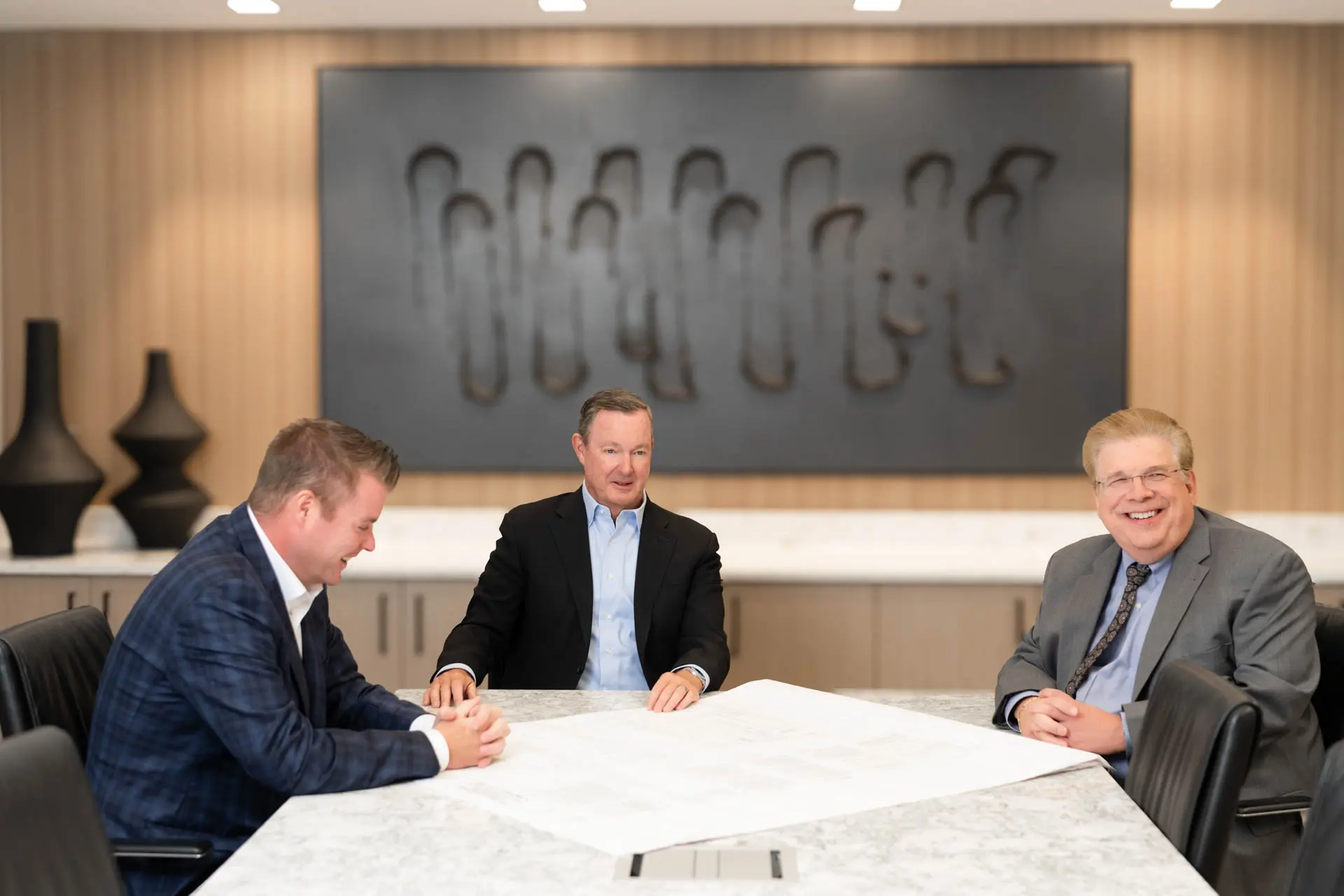 Three business professionals meeting around architectural plans in a conference room.